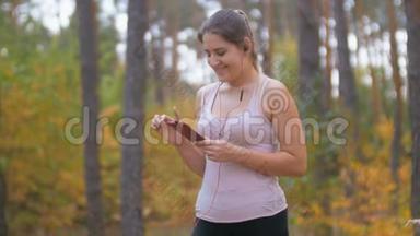美丽的年轻女子在森林慢跑前选择智能<strong>手机音乐</strong>曲目